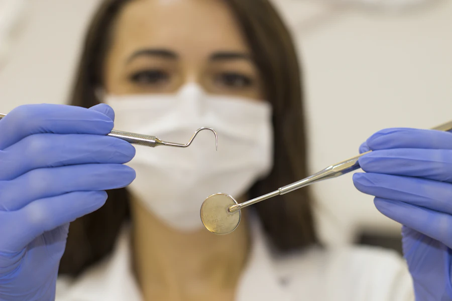 Dentista com máscara e luvas segurando instrumentos esterilizados